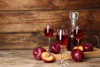 Delicious plum liquor and ripe fruits on wooden table. Homemade strong alcoholic beverage