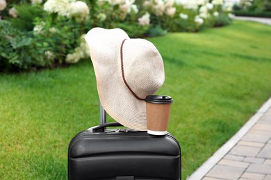 Paper cup of hot coffee and beige hat on suitcase outdoors. Takeaway drink