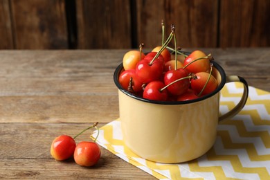 Photo of Sweet red cherries in enameled mug on wooden table, space for text