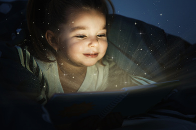 Cute little child reading magic book in darkness