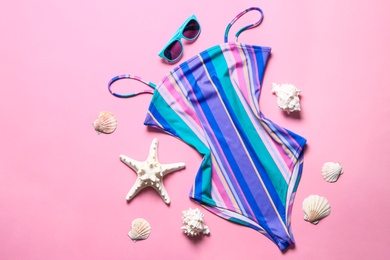 Flat lay composition with one-piece swimsuit, sunglasses and shells on color background