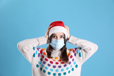 Photo of Shocked woman in Santa hat and medical mask on light blue background