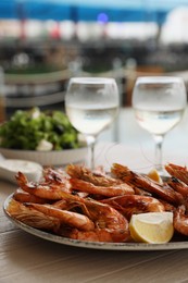 Photo of Plate of delicious cooked shrimps served with lemon and wine at table outdoors