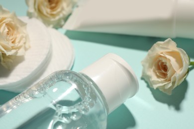 Photo of Bottle of micellar cleansing water, cotton pads and flowers on turquoise background, closeup