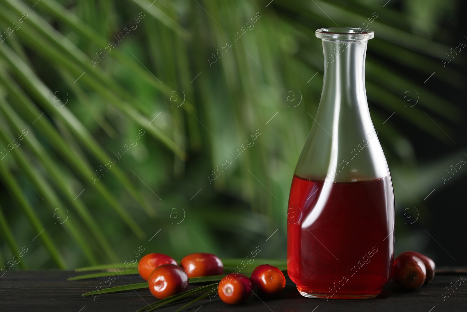 Photo of Palm oil in glass bottle, tropical leaf and fruits on wooden table. Space for text