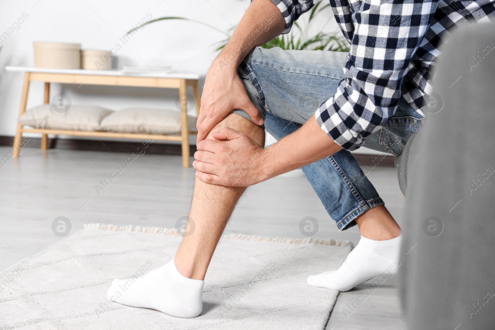 Photo of Man rubbing sore leg on sofa at home, closeup