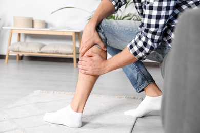 Photo of Man rubbing sore leg on sofa at home, closeup