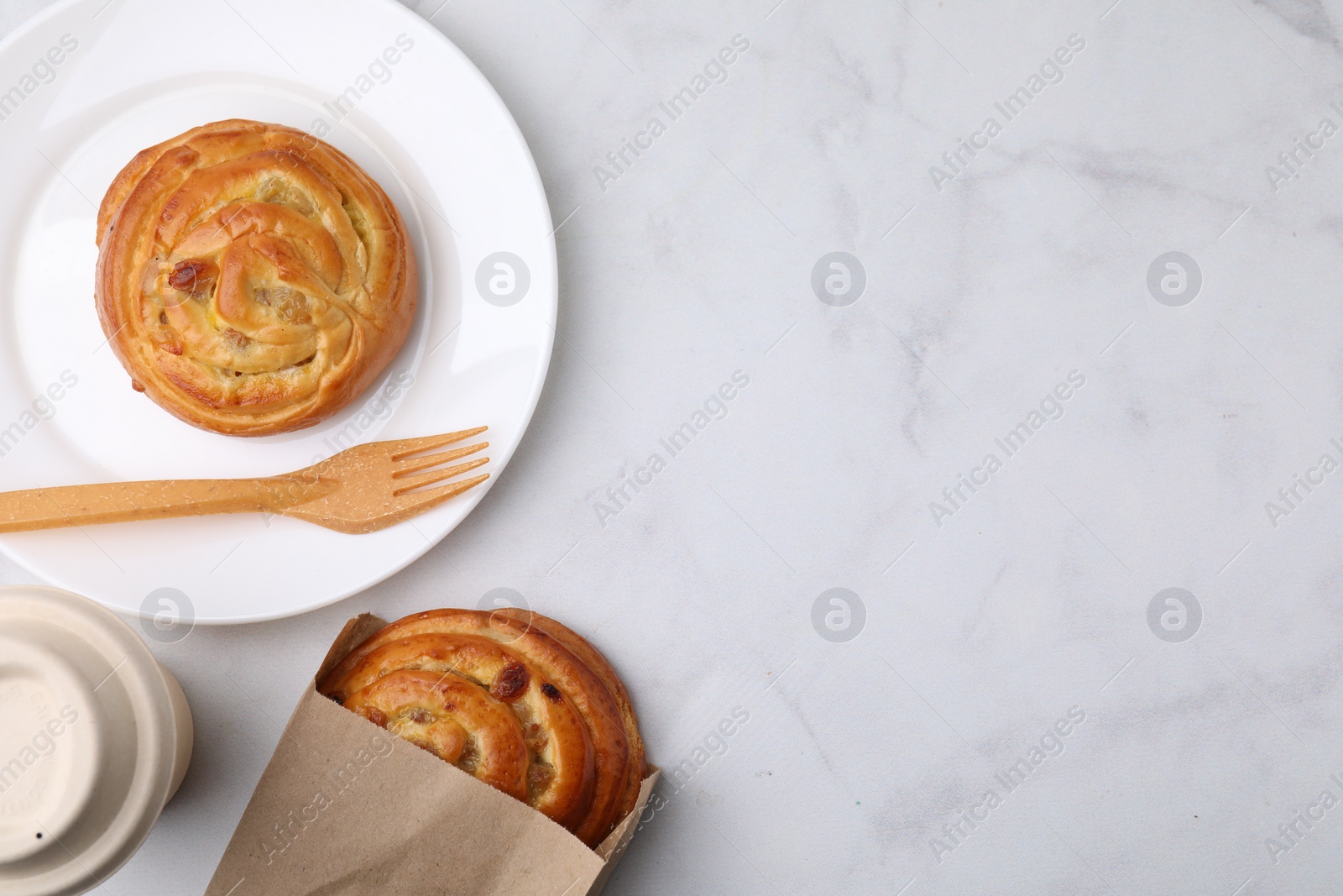 Photo of Paper bag with delicious rolls on white marble table, flat lay and space for text. Sweet buns