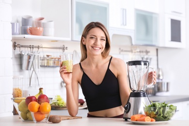 Photo of Young woman with glass of tasty healthy smoothie at table in kitchen