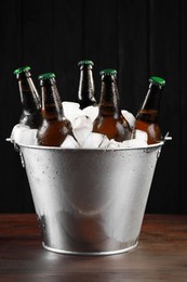 Photo of Metal bucket with bottles of beer and ice cubes on wooden table
