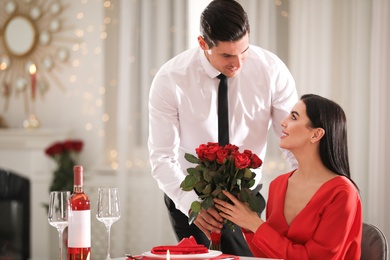 Photo of Man presenting roses to his beloved woman in restaurant. Romantic Valentine's day dinner