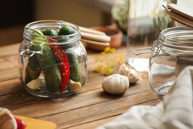 Photo of Glass jar with fresh cucumbers and other ingredients on wooden table, closeup. Pickling vegetables