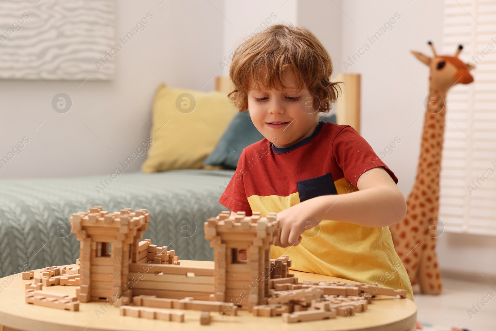 Photo of Cute little boy playing with wooden construction set at table in room. Child's toy