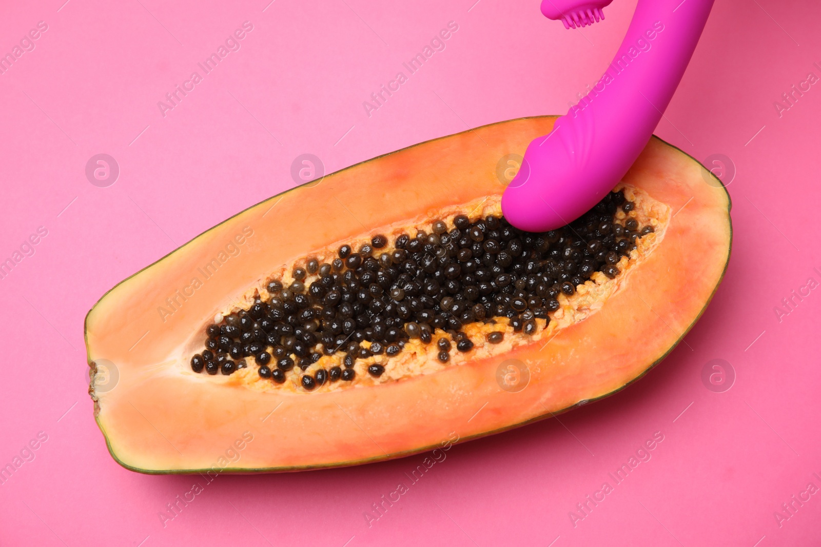 Photo of Half of papaya and purple vibrator on pink background, top view. Sex concept