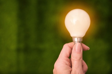 Photo of Woman holding lamp bulb against green background, closeup. Space for text