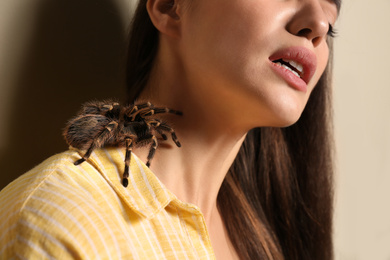 Photo of Young woman with tarantula on beige background, closeup. Arachnophobia (fearspiders)