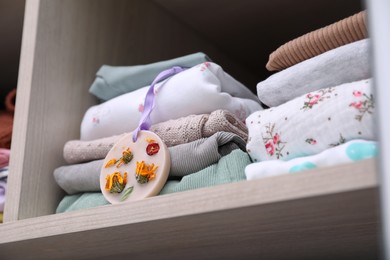 Beautiful scented wax sachet near stack of clothes on shelf in wardrobe, closeup