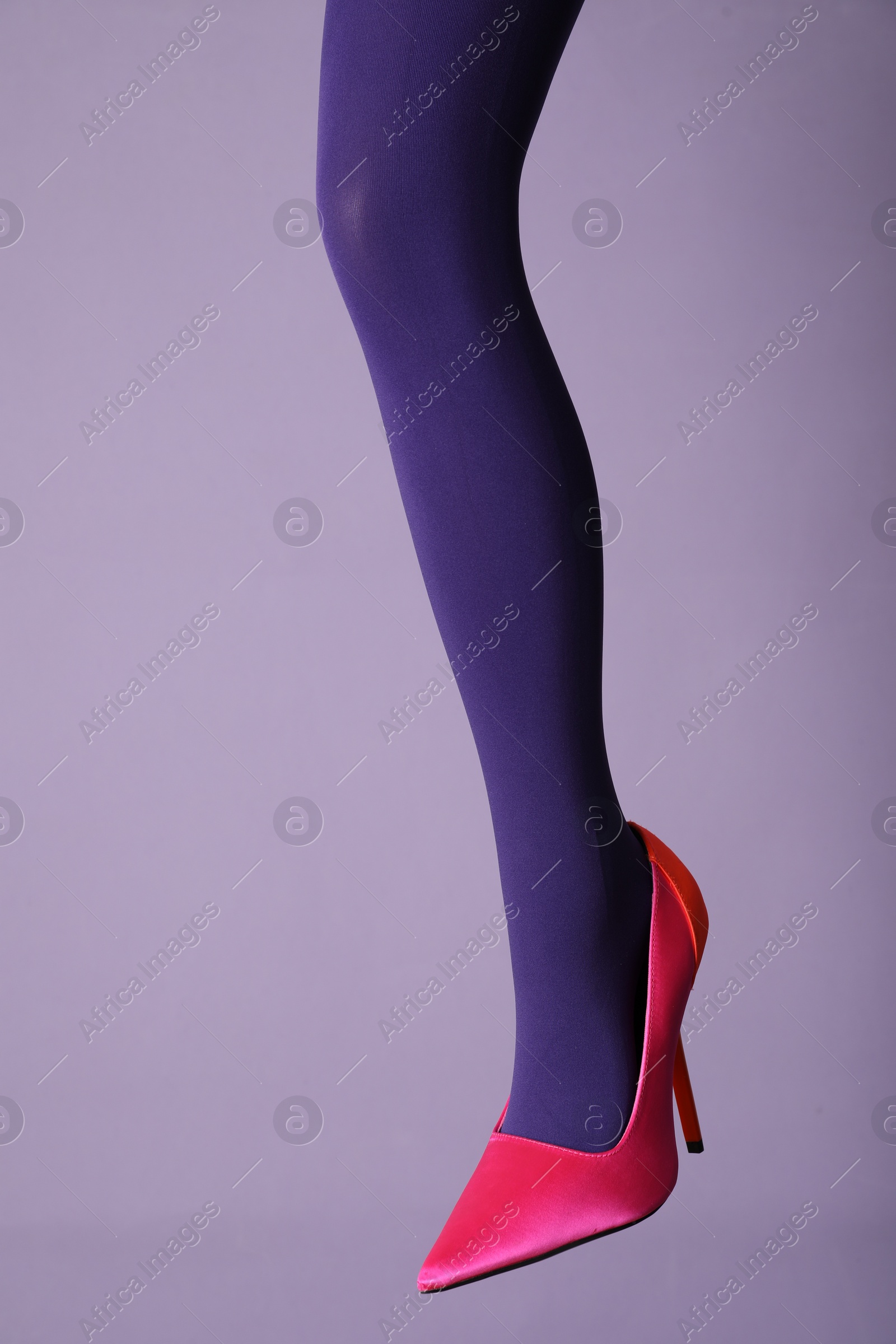 Photo of Woman wearing bright tights and high heel shoe on violet background, closeup