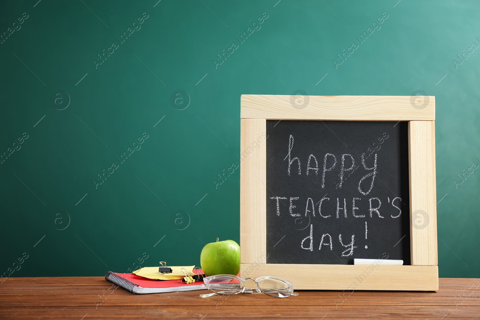 Photo of Little blackboard with inscription HAPPY TEACHER'S DAY and eyeglasses on table