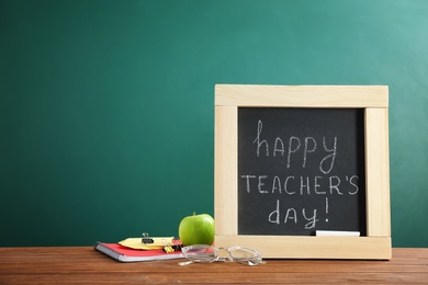 Little blackboard with inscription HAPPY TEACHER'S DAY and eyeglasses on table