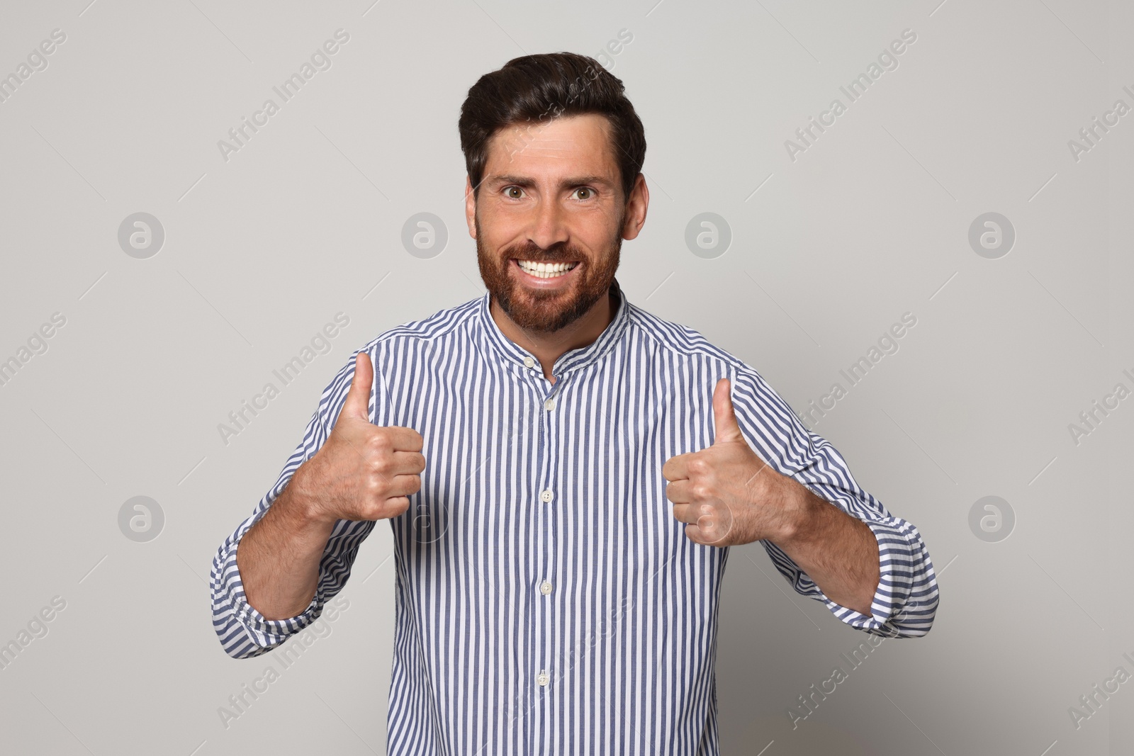 Photo of Handsome bearded man showing thumbs up on light grey background