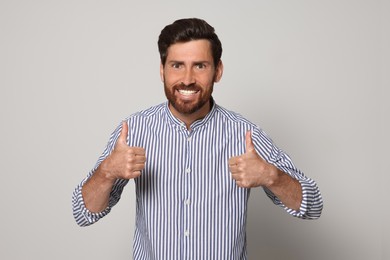 Handsome bearded man showing thumbs up on light grey background
