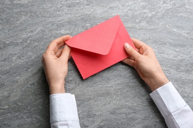 Woman holding red paper envelope on grey background, closeup