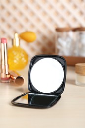 Photo of Stylish pocket mirror and cosmetic products on beige table