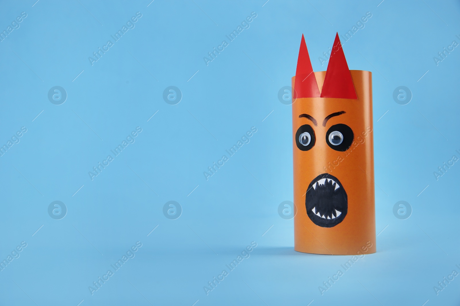 Photo of Funny orange monster on light blue background, space for text. Halloween decoration