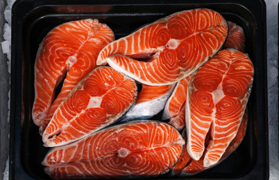 Photo of Steaks of fresh fish in container, top view