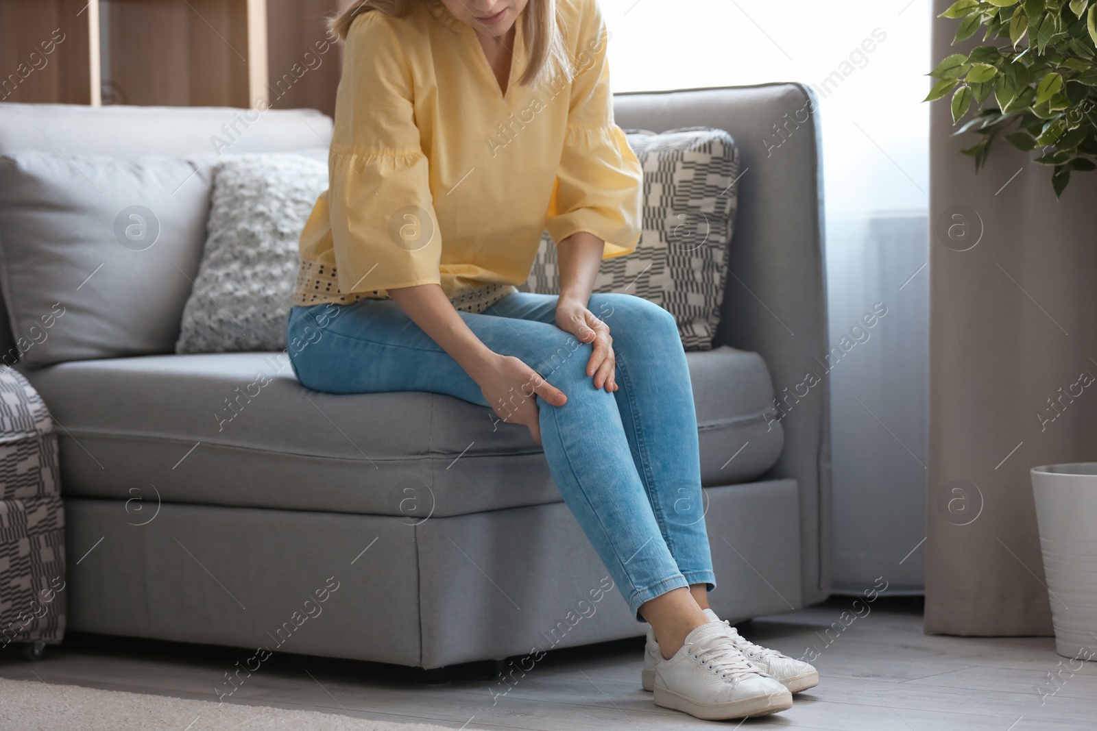 Photo of Young woman suffering from knee pain at home