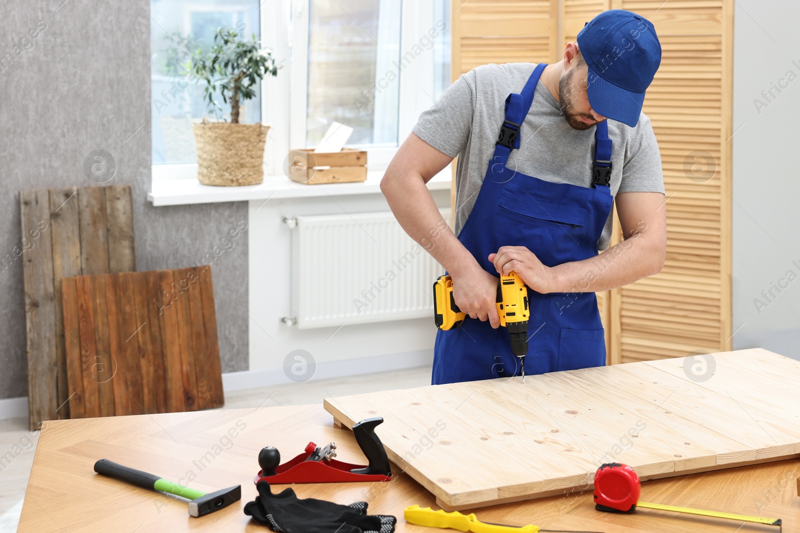 Photo of Young worker using electric drill at table in workshop