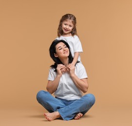 Beautiful mother with little daughter on beige background. Space for text