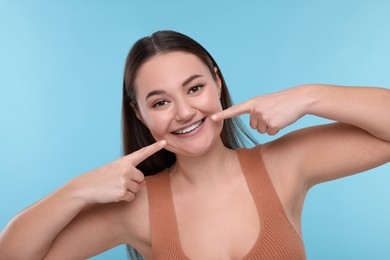 Happy woman showing braces on her teeth against light blue background