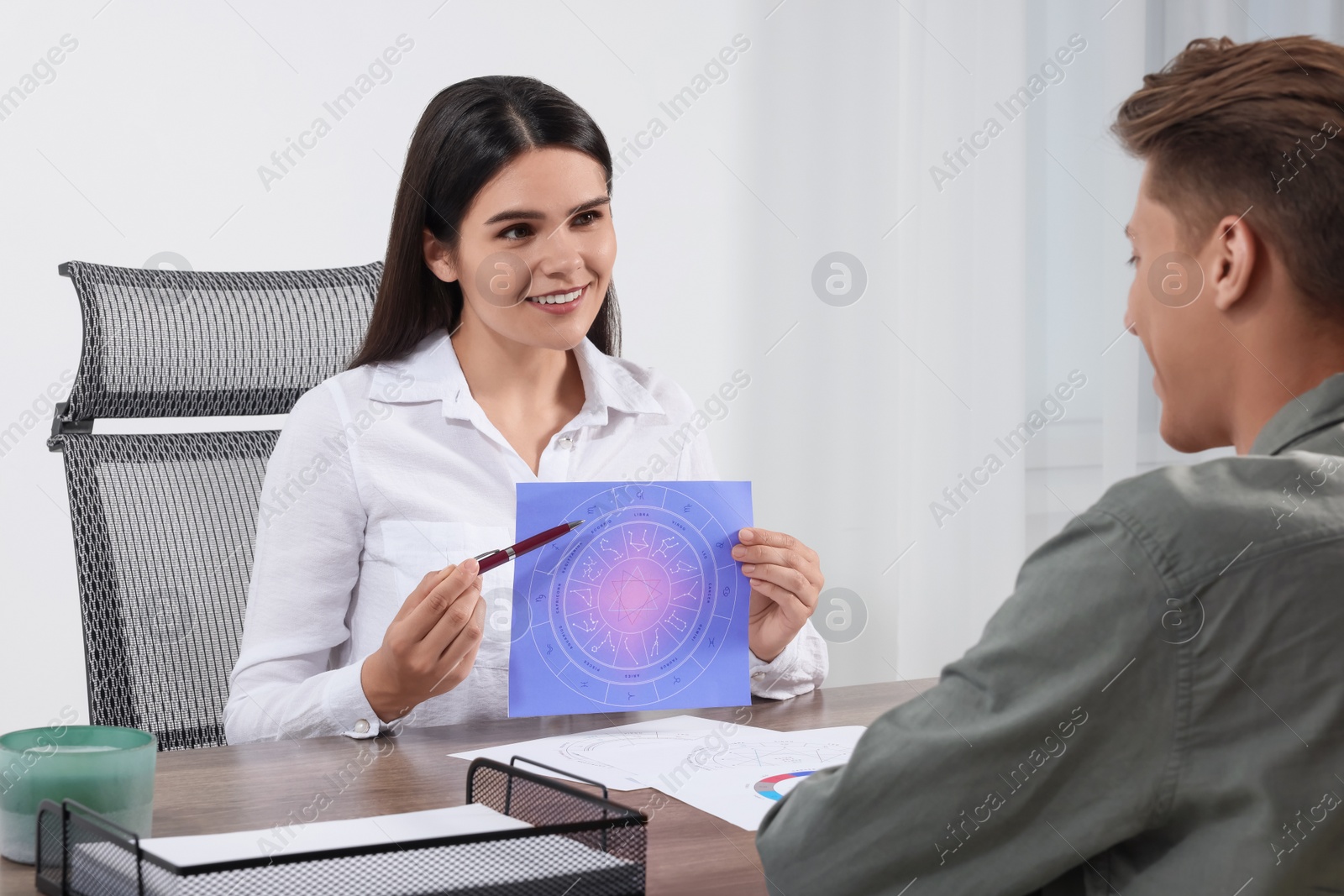 Photo of Astrologer showing zodiac wheel to client at wooden table indoors