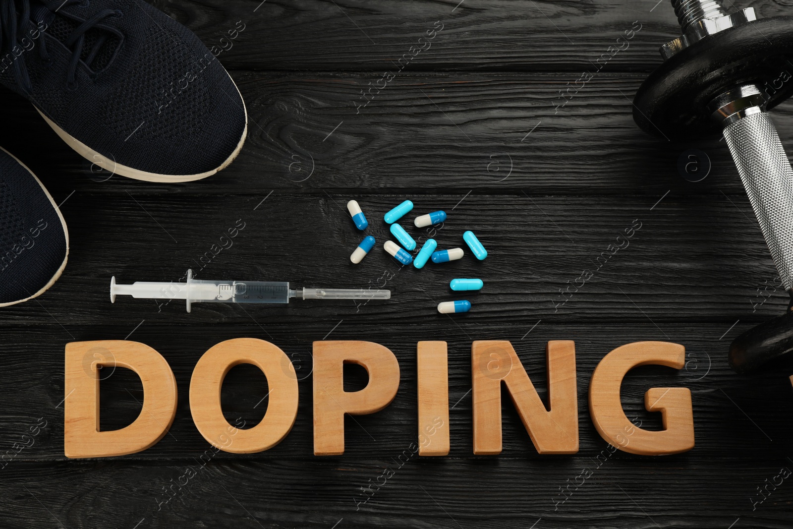Photo of Word Doping, sport shoes, dumbbell and drugs on black wooden background, flat lay