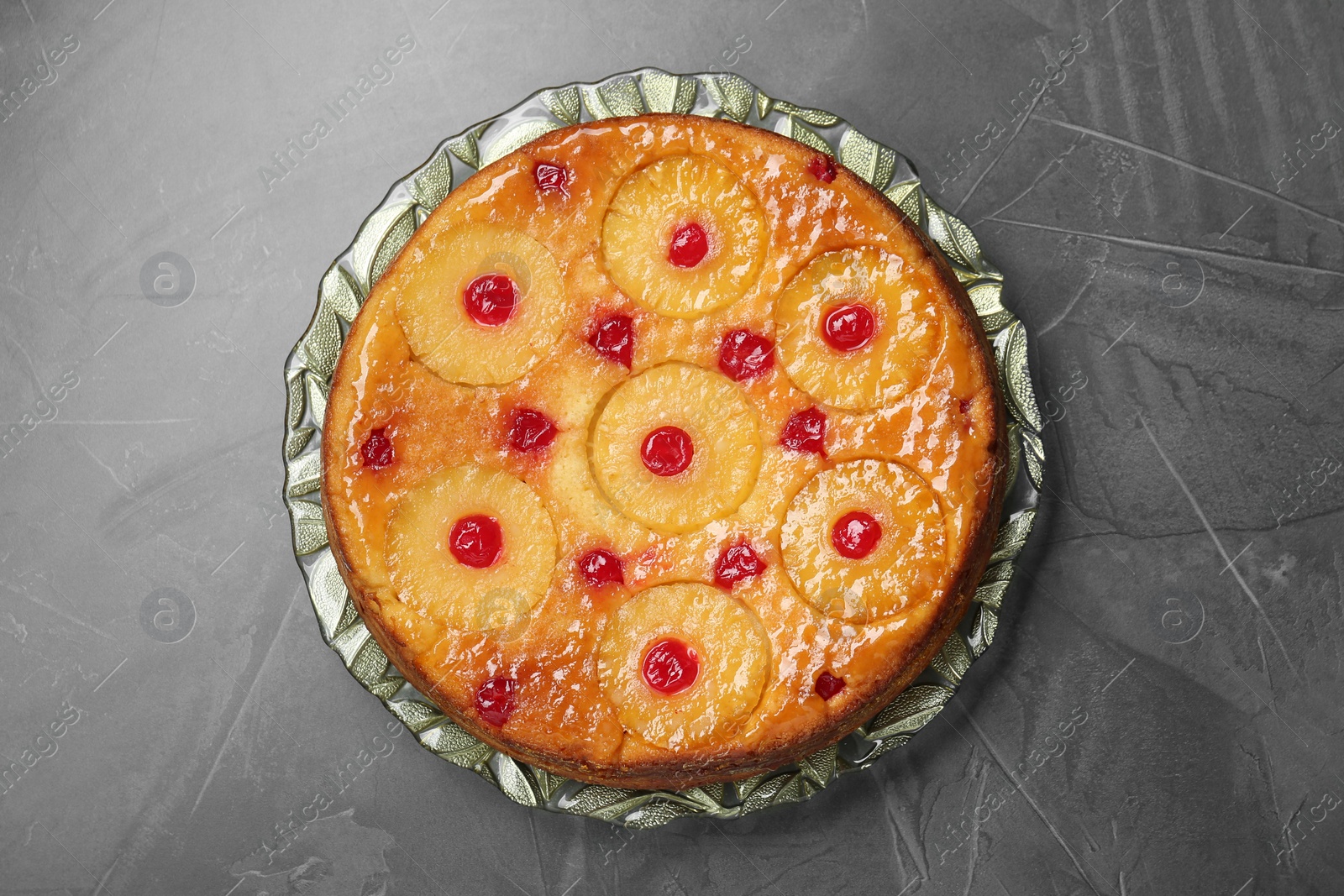 Photo of Plate with tasty pineapple cake on grey textured table, top view