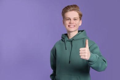 Photo of Teenage boy showing thumb up on purple background. Space for text