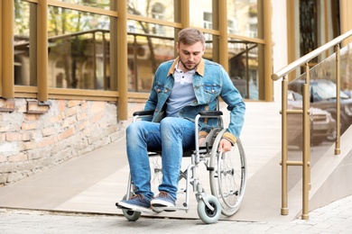 Young man in wheelchair using ramp at building outdoors