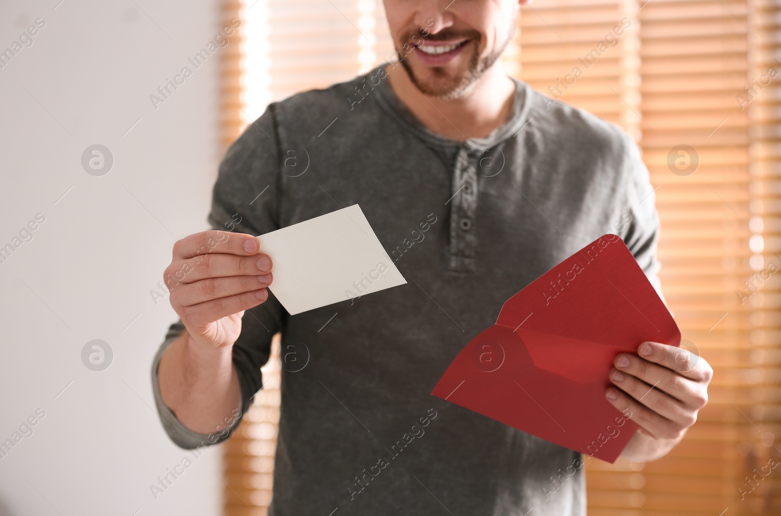 Photo of Man holding envelope with blank greeting card indoors. closeup