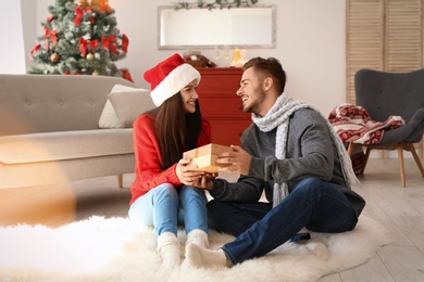 Young man giving gift box to girlfriend at home. Happy couple celebrating Christmas