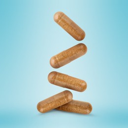 Vitamin. Capsules falling on light blue gradient background