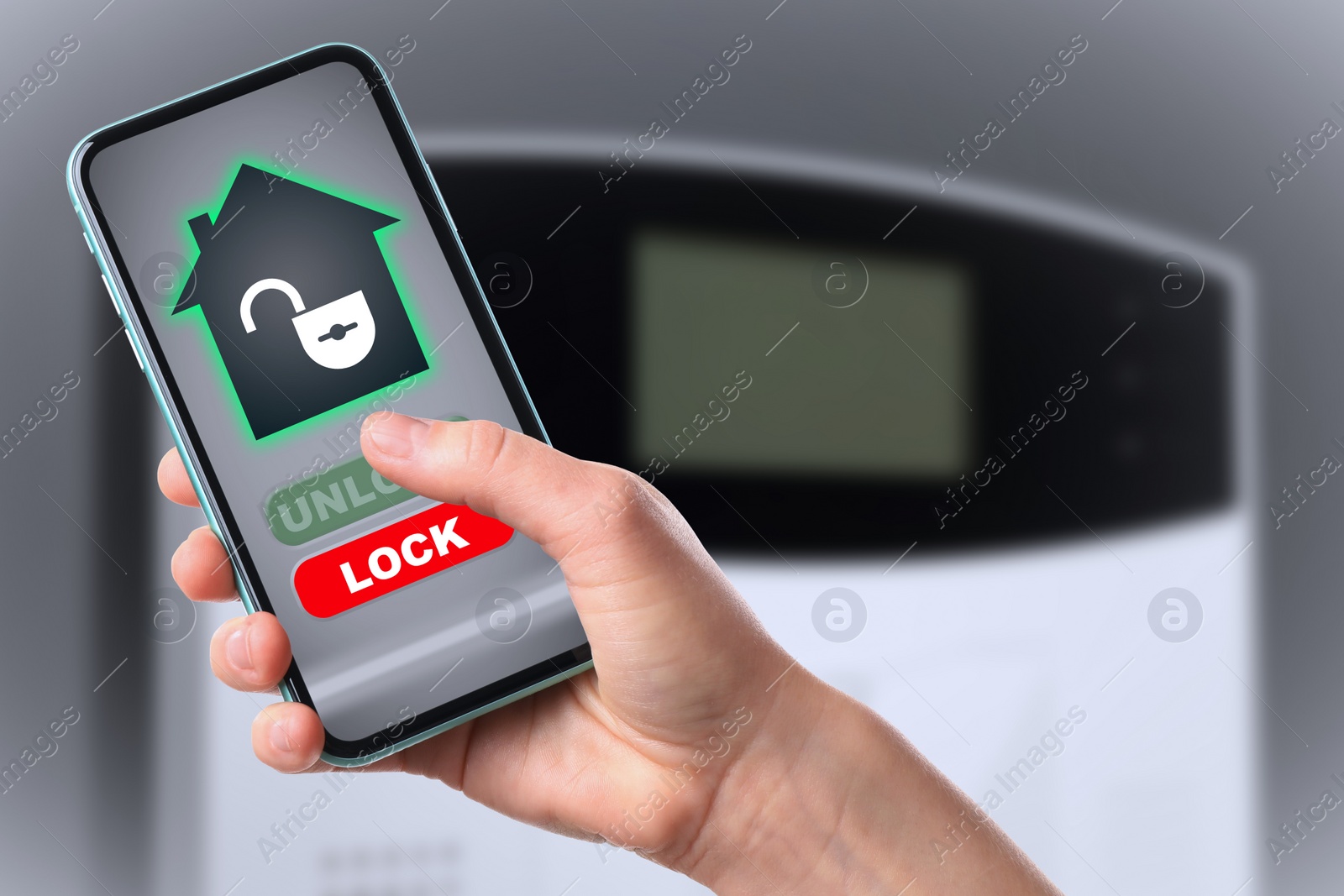 Image of Woman operating home alarm system via mobile phone against grey wall with security control panel, closeup. Application interface on device screen