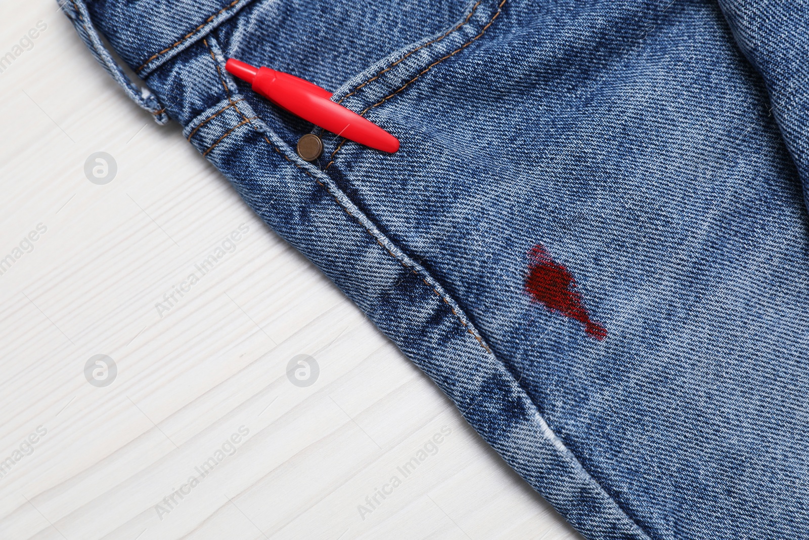 Photo of Jeans with stain of red ink and pen in pocket on wooden table, top view. Space for text