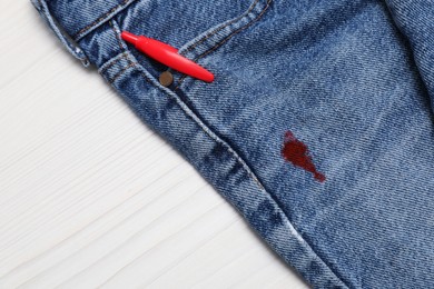 Photo of Jeans with stain of red ink and pen in pocket on wooden table, top view. Space for text