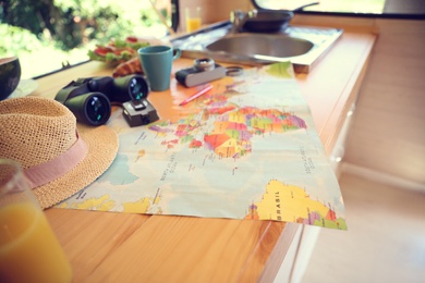Photo of World map and travel accessories on wooden table in motorhome. Summer trip