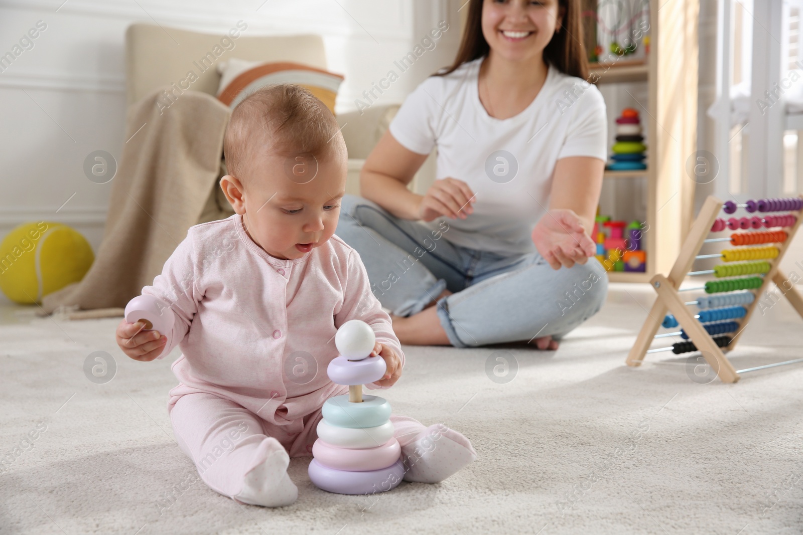 Photo of Cute baby girl playing with toy pyramid and mother on floor at home