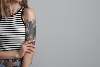 Photo of Beautiful woman with tattoos on body against grey background, closeup. Space for text