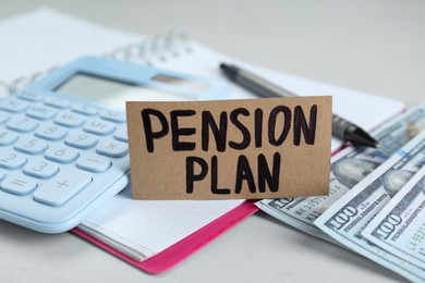 Photo of Card with words Pension Plan, banknotes, calculator and notebook on white table, closeup