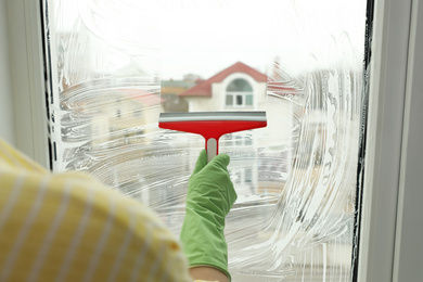 Photo of Woman cleaning window with squeegee indoors, closeup